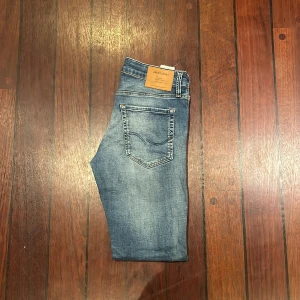 Blå jeans från Jack & Jones - Snygga blå jeans från Jack & Jones. Jeansen har klassisk femficksdesign, ljus tvätt med slitningar och detaljerade sömmar. Perfekta för dig som gillar en smalare passform och vill ha en modern look.