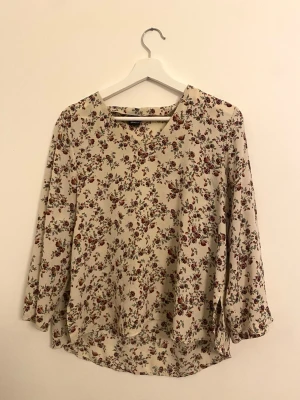 Blommig blus i beige – luftig & feminin - Säljer en fin blommig blus i beige ton med små blommor i varma färger. Blusen har V-ringning, 3/4-ärm och en lätt, luftig passform som faller fint. Perfekt till vardag.