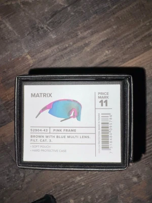 Bliz glasögon - Bilderna visar ett par sportglasögon från Bliz Matrix med rosa båge och blåtonade linser, samt tillhörande förvaringsbox och mjuk påse. Ingen väst syns på bilderna.