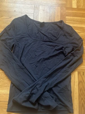 Grå långärmad topp med rund hals - En enkel grå långärmad topp med rundad halsringning. Tunn och mjuk i materialet, perfekt att ha som basplagg eller under en jacka. Stilren och passar till många olika outfits.