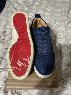 Marinblåa Christian Louboutin sneakers - Säljer ett par marinblåa sneakers från Christian Louboutin med ikonisk röd sula och coola nitar på tån. Perfekt för dig som vill sticka ut med lyxig look. Skick 7.8/10 Skriv om du har några frågor.