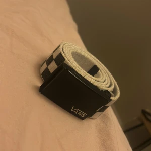 Svartvit rutig Vans bälte - Säljer ett snyggt bälte från Vans med klassiskt svartvitt rutigt mönster och svart spänne med Vans-logga. Bältet är gjort i slitstark bomull och passar perfekt till jeans eller shorts för en cool streetstil.