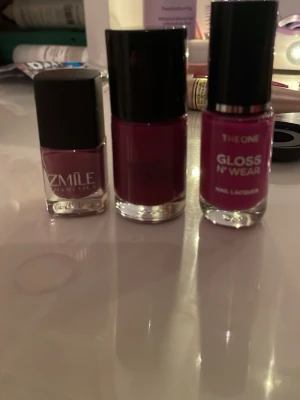 Tre nagellack i rosa och vinrött - Säljer tre snygga nagellack i olika nyanser av rosa och vinrött. Zmile Cosmetics har en matt mörkrosa ton, The One Gloss N' Wear är klarrosa och det tredje är djupt vinrött. Alla kommer i glasflaskor med svarta lock.