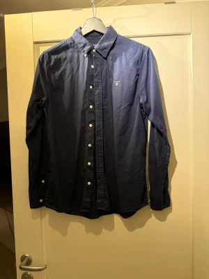 Mörkblå skjorta från GANT - Snygg mörkblå skjorta från GANT med klassisk krage och vita knappar framtil. Bredd 39 Längd 64