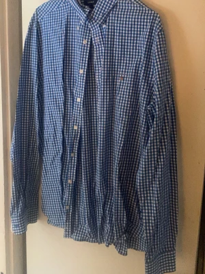Blårutig skjorta från GANT XL - Säljer en fräsch blårutig skjorta från GANT i storlek XL. Skjortan har klassisk krage, vita knappar och ett stilrent rutmönster i blått och vitt. Materialet är mjuk bomull och passformen är slim. Perfekt för dig som gillar preppy stil!