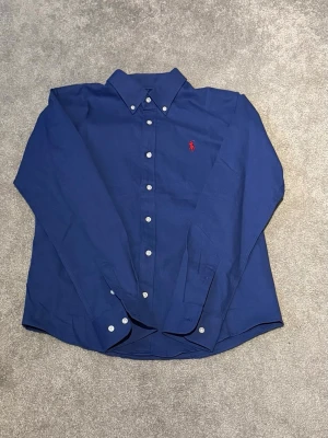 Ralph Lauren Skjorta - Säljer en helt oanvänd polo skjorta från Ralph lauren i färgen blå. Skick: 10/10. Nypris: 1399kr. Storlek: M passa S. Skriv vid funderingar!