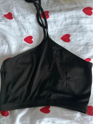 Svart ribbad linnetopp med smala band - Säljer en svart ribbad linnetopp med smala axelband som knyts i nacken. Toppen har en croppad passform och är tillverkad i ett mjukt, stretchigt material som känns bekvämt mot huden. Perfekt till sommaren eller för att styla lager på lager.