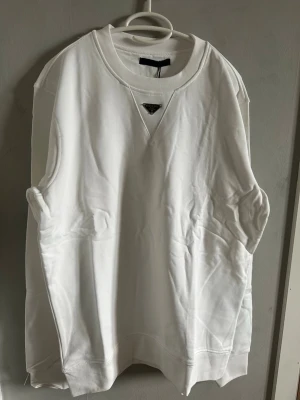 Vit sweatshirt från Prada.  - Vit Prada sweatshirt i storlek M. Helt ny aldrig använd. Metall logo på bröstet. 