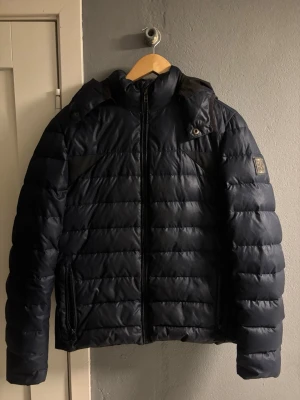 Mörkblå pufferjacka Calvin Klein Jeans - Snygg mörkblå pufferjacka från Calvin Klein  med huva och dragkedja framtill.  Perfekt för kalla dagar och har en clean look som funkar till många stilar.pris kan diskuteras 