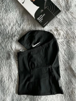 Svart ski mask  - Ski masken är tillverkad i ett syntetmaterial som andas och har en tight passform. Perfekt för träning och sportaktiviteter. Snygg detalj med Nike Pro-märke nedtill.
