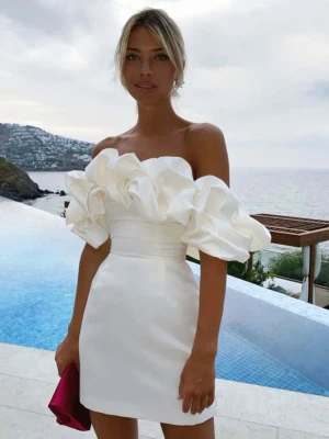 Studentklänning  - Superfin vit axelbandslös kortklänning i glansigt satinliknande material. Klänningen har stora volangdetaljer upptill som ger en riktigt statement-look. Sitter tajt i midjan och har en elegant, stilren siluett. Perfekt inför studenten