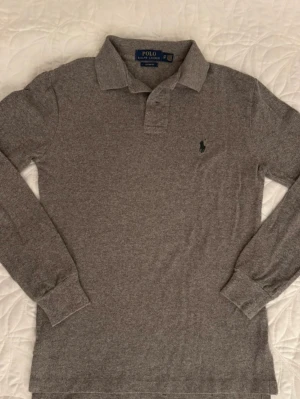 Grå långärmad pikéskjorta Polo Ralph Lauren - Säljer en grå långärmad pikéskjorta från Polo Ralph Lauren i custom fit. Storlek XS, mycket fint skick (knappt använd) pris kan sänkas lite vid snabb affär