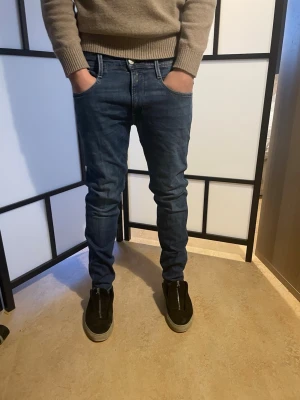 Replay Anbass blå jeans slim fit - Säljer ett par snygga Replay Anbass jeans i klassisk blå tvätt. Modellen är slim fit med normal passform och raka ben. Jeansen har fem fickor, tydliga sömmar och Replay-logga på fickan. Materialet är slitstarkt jeans i bomull med lite stretch för extra komfort.