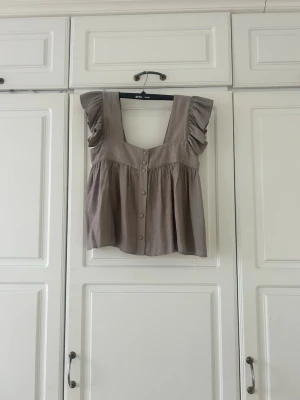 Beige blus med volang från Zara💕💕 - Säljer en beige blus från Zara i storlek XS. Blusen har breda axelband med volangdetaljer och knappar framtill. Modellen är luftig och har en lätt rynkad nederdel som ger en avslappnad look. Perfekt för vår och sommar!
