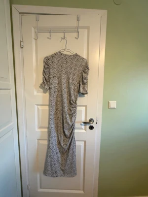 Blommig långklänning med puffärm - Säljer en  långklänning med blommig mönster på vit botten. Klänningen har puffiga kortärmar och en rynkad detalj längs sidan som ger en cool siluett. Från Lindex. Aldrog använt.