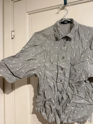 Grå/grön prickig skjorta från Bik Bok - Säljer en grå skjorta från Bik Bok i storlek XS med vita prickar. Skjortan har klassisk krage, korta ärmar och knäppning framtill. Den är lite kortare och boxigare i modellen.