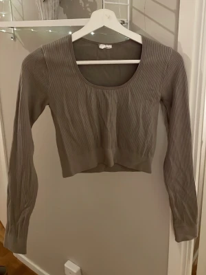 Beige ribbad croppad topp - Säljer en beige croppad topp med ribbad struktur och lång ärm. Toppen har en rundad halsringning och är tillverkad i ett mjukt, stretchigt material som sitter snyggt på kroppen. Perfekt att använda till träningen. 