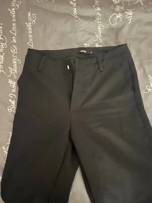 Svarta kostymbyxor från Bik Bok - Svarta kostymbyxor från Bik Bok i klassisk rak modell med bälteshällor och diskreta bakfickor. Byxorna har en stilren look och är gjorda i ett mjukt material som känns skönt mot huden. Perfekta för dig som gillar en clean och enkel stil.