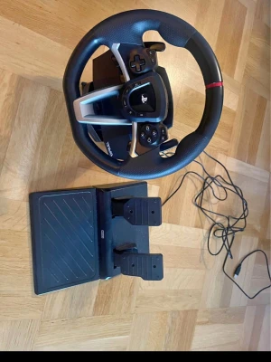 Hori Racing Wheel Apex - Hori Racing Wheel Apex med pedaler, kompatibel med PlayStation. Perfekt för racingspel, med responsiva knappar och realistisk känsla. USB-anslutning, lätt att installera. Produkten ser ut att vara i gott skick utan synliga defekter eller slitage.