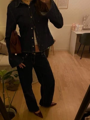 Brun kuvertväska i skinn  - Snygg brun kuvertväska med flätad struktur och unik form. Väskan är tillverkad i skinn och har ett coolt, trendigt utseende som sticker ut. Perfekt att bära under armen och passar till många olika outfits.