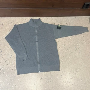 Grå stickad kofta från Stone Island - Säljer en grå stickad kofta från Stone Island med hel dragkedja och ribbad struktur. Storlek L men passar mig som är 185cm så är du M passar den nog också. Priset är diskuterbart!