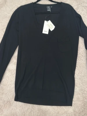 Svart v-ringad tröja Filippa K - Svart långärmad tröja från Filippa K med v-ringning och liten bröstficka. Tröjan har en stilren och enkel design, perfekt för dig som gillar minimalistiskt mode. Materialet är mjukt och skönt bomull, vilket gör den bekväm att bära hela dagen.