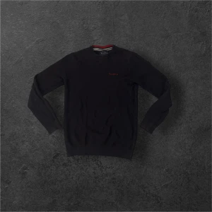 stickad tröja  - Svart stickad tröja från Bondelid med rund hals och diskret röd broderad logga på bröstet. Insidan av kragen har en snygg randig detalj i rött, vitt och grönt. Tröjan har långärmade ribbade muddar och en klassisk, normal passform. Bara att höra av sig vid funderingar!🔥                                   (Priset är inte hugget i sten så kom med förslag)