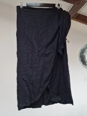 Black wrap skirt - Black wrap skirt that also has a partially elastic waistband. You fasten it by a button and then a tie. Soft and comfortable fabric in 55% viscose, 45% linen. Length: 76 cm 