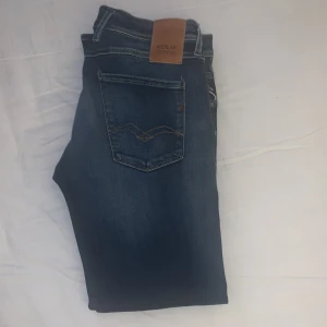 Replay Anbass Hyperflex jeans blå 32/30 - Nypris 1899kr Snygga Replay Anbass Hyperflex jeans i mörkblå tvätt med klassisk femficksdesign och subtila slitningar. Stretchigt material för skön passform och smal siluett. Läderpatch med Replay-logga bak. Perfekt för dig som gillar stilrena jeans med modern känsla.