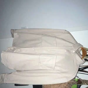 Beige overshirt från C&A - Stilren beige overshirt från C&A med klassisk krage, stora bröstfickor och knäppning framtill. Jackan är i mjuk bomull och har en clean look som passar perfekt till lager-på-lager. Enkel och snygg design med lång ärm och rak passform.
