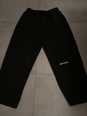 Svarta mjukisbyxor från YoungLA - Svarta mjukisbyxor från YoungLA med broderad logga på benet och bakfickan. Byxorna har elastisk midja och en loose passform med raka ben. Perfekta för chill eller träning, riktigt sköna och stilrena. Byxorna har också en go slitning vid midjan och runt anklarna som är riktigt fett 