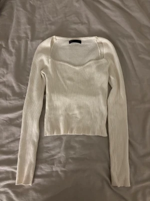 Vit ribbad croppad topp - Säljer en vit, ribbad och croppad topp med lång ärm och snygg sweetheart-ringning. Toppen har en figurnära passform och är tillverkad i mjukt, stretchigt material som känns skönt mot huden. Perfekt att styla med jeans eller kjol för en trendig look.