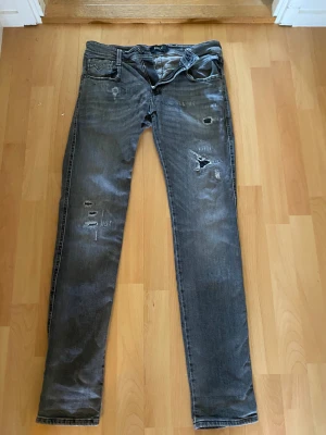 Replay Anbass grå slitna jeans - Säljer ett par Replay Anbass jeans i grå tvätt med slitningar och hål för en riktigt edgy look. Slim fit med normal midja och klassiska fem fickor. Perfekta för dig som gillar streetstyle och vill ha ett par jeans som sticker ut.