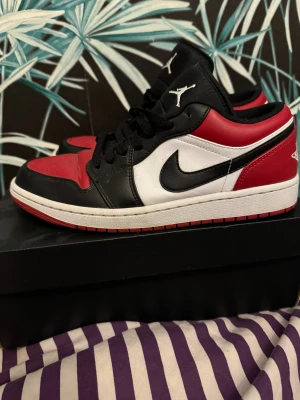 Nike Air Jordan 1 Low svart/röd/vit - Nike Air Jordan 1 Low sneakers i klassisk svart, röd och vit färgkombination. Skorna har en låg siluett, snörning och rund tå. Ikonisk Swoosh på sidan och Air Jordan-logga på hälen. Tillverkade i skinn med platt sula och perforerad tåbox för extra stil. Skick 9/10 och nypris på dessa är 2299kr som ni ser på sista bilden och säljer de för 1199: vid snabb affär kan jag tänka mig gå ner.