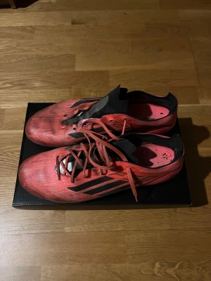 Röda Adidas fotbollsskor med väska - Säljer ett par röda Adidas fotbollsskor med svarta detaljer och snörning. Endast 1 snöre då andra har gått sönder därav priset. Enkelt att bara lägga till ett annat snöre! NY PRIS 3199. Box och väska medföljer