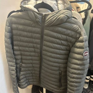 Grå dunjacka från Colmar - Säljer en snygg grå dunjacka från Colmar i mycket bra skick. Jackan har en quiltad design med dragkedja framtill och en mysig huva, den har ett litet hål i högra jack fickan, inget man ser utifrån, därmed är priset billigare 