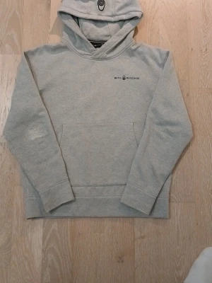 Sail Racing Hoodie-Grå - Säljer en grå sail racing heavy hood då jag inte använder den längre. Den passar perfekt för dig som vill bli varm under vintern! Den är använd några gånger men de enda slitaget finns med på bilderna men kan fixas, annars är den stilren!
