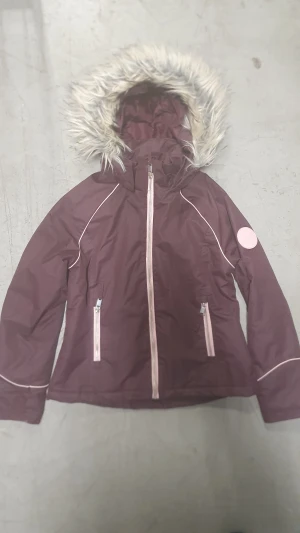 Vinterjacka - Snygg lila vinterjacka från H&M med fuskpäls på huvan och ljusrosa detaljer. Jackan har dragkedja framtill, två fickor med dragkedja och ett coolt rosa märke på ärmen med texten 'Support Your Local Girl Crew'. Perfekt för kalla dagar!