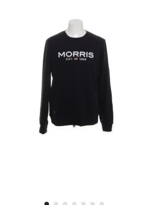 Svart sweatshirt från Morris, storlek L - Svart sweatshirt från Morris med vit logotyp och text 'MORRIS EST. 1968' på bröstet. Tröjan har rund hals, långa ärmar och ribbade muddar vid ärmslut och nederkant. Tillverkad i mjuk bomullsmix som är skön att bära.