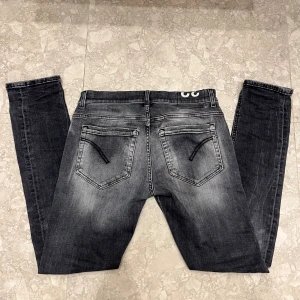 Dondup george - Snygga svarta jeans från Dondup med slitna detaljer och tvättad look. Modellen är skinny med normal passform och har klassiska fem fickor, dragkedja och knapp framtill. Materialet är stretchigt jeans och bakfickorna har svarta broderade detaljer.