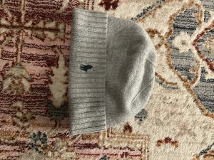 Grå stickad mössa från Polo Ralph Lauren - Snygg grå stickad mössa från Polo Ralph Lauren med klassisk ribbad kant och den ikoniska mörkblå polospelaren broderad framtill. Perfekt accessoar för kyliga dagar och enkel att matcha med din stil.