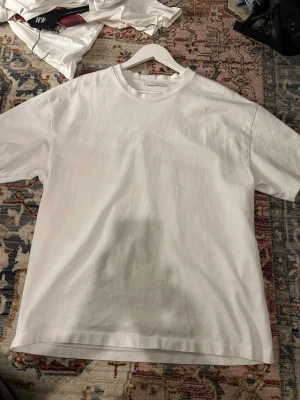 Vit basic t-shirt från Zara, storlek L - En clean och klassisk vit t-shirt från Zara i storlek L. Modellen har rund hals och korta ärmar, perfekt för en enkel och stilren look. Tillverkad i mjuk bomull som känns skön mot huden. Passar dig som gillar minimalistisk stil.