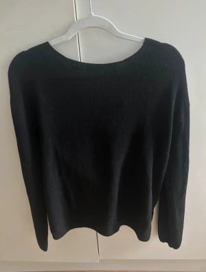 Svart stickad tröja med omlottdetalj i ryggen - Säljer en svart stickad tröja med snygg omlottdetalj i ryggen. Tröjan har ärm och en lite lösare passform. Perfekt för dig som gillar stilren men ändå trendig look. Passar till många olika outfits och är superenkel att matcha