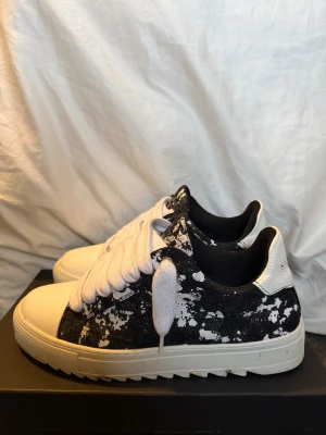 Numeris svartvita sneakers med mönster - Säljer ett par feta sneakers från Numeris i storlek 42,5, passar även storlek 43. Ny pris 2,400kr Skorna har svart och vitt splattermönster, breda vita snören och vit platt sula med räfflad undersida. Ovandelen är i textil och detaljer i vitt skinn på häl och tå. Perfekt för dig som vill sticka ut med en unik look.