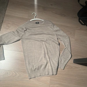 Beige merinoulltröja från H&M - Snygg beige tröja från H&M i merinoullsblandning. Enkel och stilren design med rund hals och långa ärmar. Perfekt för dig som gillar en clean look och vill ha något mjukt och skönt till hösten eller vintern. Passar lika bra till jeans som till kostymbyxor.