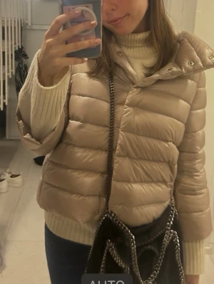Beige pufferjacka från Herno - Säljer en beige pufferjacka från Herno Iconico med glansig finish och medium insulation. Jackan har en hög krage, tryckknappar och quiltad design. Perfekt för dig som vill ha en snygg och varm jacka med lite oversized passform. Storlek it40 men passar xs-s