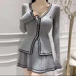 Set kofta Knitted Grå ribbad med knappar och kjol - Superfin grå ribbad klänning med svart kant och v-ringning. Klänningen har långa ärmar, knappar framtill och en plisserad kjol med kontrastdetaljer. Snyggt figurnära passform och coolt college-vibe. Perfekt för dig som gillar stilrena detaljer och modern look.