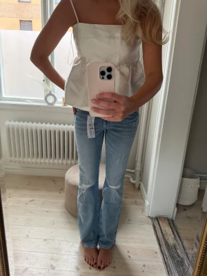 Ljusblå bootcut jeans med slitningar - Säljer ett par ljusblå jeans med bootcut passform och snygga slitningar vid knäna och framtill. Jeansen har klassiska fem fickor, knapp och dragkedja framtill samt en lätt tvättad look. Perfekta för dig som gillar en avslappnad och trendig stil. Lapp kvar 