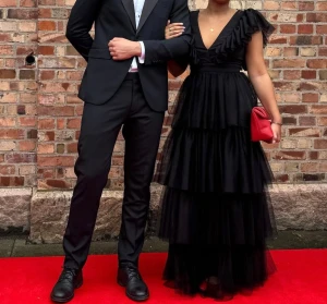 Balklänning - Säljer en svart balklänning med volanger och djup v-ringning, öppen rygg, passar mig som kan ha både S/M. Användes på min studentbal och passar perfekt till röda mattan!