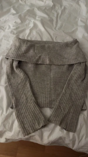 Ribbad offshoulder tröja från H&M - Säljer en ribbad, ljusgrå offshoulder stickad tröja från H&M i storlek S. Tröjan har långa ärmar och en bred krage som sitter snyggt över axlarna. Perfekt för dig som gillar en chill och trendig look. Den sitter tightare på magen. Andvänd fåtal gånger. En grå beige färg.